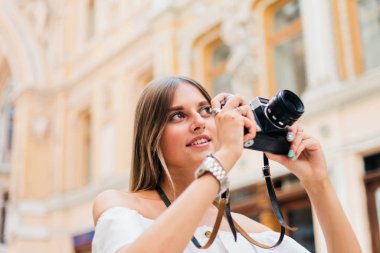 Kentsel eski mimariye poz verirken elinde retro kamerayla genç ve çekici bir turist kadın. Yeni yerler keşfet