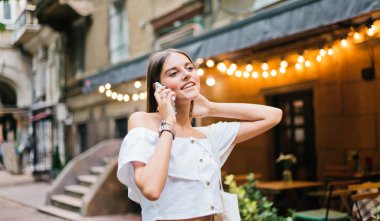 Neşeli, karizmatik bir kadın akşam vakti eski şehir caddesinde yürürken telefonla konuşuyor.