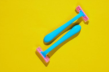 Sarı arka planda iki mavi plastik tıraş bıçağı. Asgari güzellik ve moda konsepti