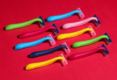 Güzellik ve moda sanatları konsepti. Kırmızı arka planda bir sürü renkli plastik tıraş bıçağı var. Minimalizm