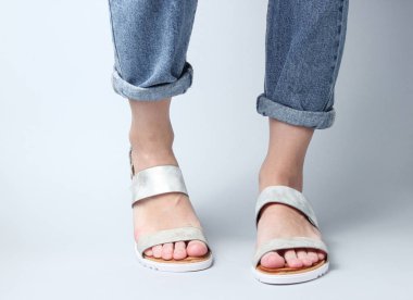 Mavi kotlu kadın bacakları ve beyaz arka planda son moda deri sandaletler. Kadınların şık yaz ayakkabıları. Minimalist moda çekimi