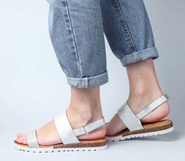 Mavi kotlu kadın bacakları ve beyaz arka planda yürüyen moda deri sandaletler. Kadınların şık yaz ayakkabıları. Minimalist moda çekimi