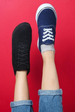 Pantolonlu, çizmeli ve kırmızı arka planda spor ayakkabılı kadın bacakları. Mevsimlik ayakkabılar. Yaratıcı moda çekimi