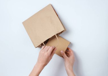 Kadın eli, karton kutuyu gri arka planda kağıt torbaya koyar. Üst görünüm