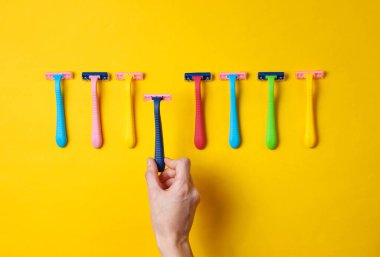 Kadın eli, sarı arka planda çeşitli renkli epilator jiletler arasından jilet seçiyor. Üst Manzara. Minimalizm güzellik kavramı