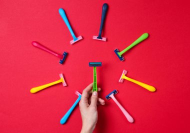 Kırmızı arka planda çeşitli renkli jiletler arasından yeşil jilet seçen bir kadın. Üst Manzara. Minimalizm güzellik konsepti. Üst görünüm