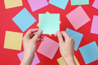 Bir çok renkli kağıt arasında kırmızı zemin üzerinde mavi not kağıdı tutan bir kadın.