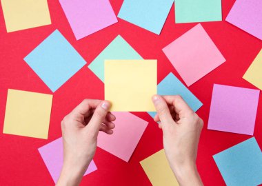 Bir çok renkli kağıt arasında kırmızı arka planda sarı not kağıdını tutan bir kadın. Üst görünüm