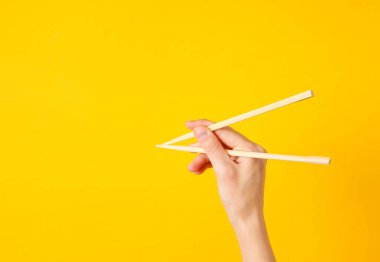 Kadın yemek çubuklarını sarı arka planda tutuyor. Minimalist gıda konsepti. Üst görünüm