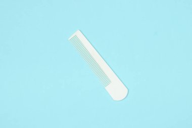 Mavi pastel arka planda beyaz plastik tarak. Saç bakımı, güzellik konsepti. Üst görünüm