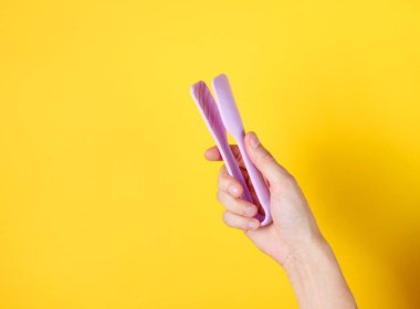 Kadın el, sarı arka planda mutfak cımbızı tutuyor. Üst görünüm