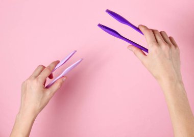 Pembe arka planda mutfak cımbızı tutan kadın elleri. Üst görünüm