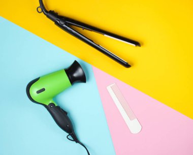 Minimalist güzellik ve moda hala hayat. Renkli arka planda saç kurutma makinesi, tarak ve saç düzleştiricisi. Üst manzara, düz uzanma
