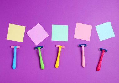 Minimalist güzellik konsepti. Epilasyon. Plastik renkli jiletler ve mor arka planda not kağıtları. Boşluğu kopyala