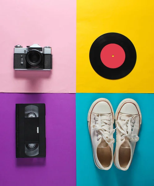 Retro still life. Old fashioned sneakers, vinyl record,  vintage film camera, video cassette on colored background. Top view. Pop art flat lay