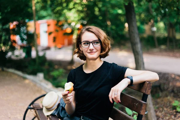 Jovem Com Cabelo Curto Óculos Senta Banco Parque Come Maçã — Fotografia de Stock