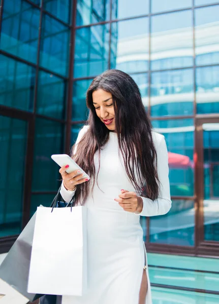 Młoda Afro Kobieta Białej Sukience Papierowymi Torbami Zakupy Używać Smartfona — Zdjęcie stockowe