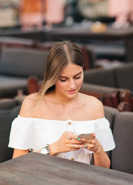 Stylowa Blondynka Trzyma Smartfona Rękach Siedząc Przy Stole Ulicznej Kawiarni — Zdjęcie stockowe