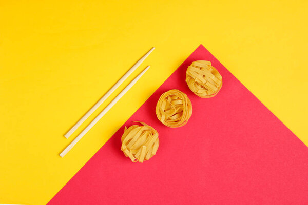 Лапша из сырой тальятелли и палочки для еды на фоне желтой красной бумаги. Минималистичная концепция питания. Вид сверху
