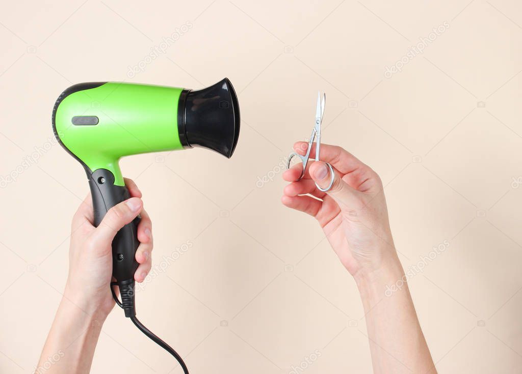 Personal care, beauty concept. Female hands holding nail scissors and hairdryer on a beige background. Top view