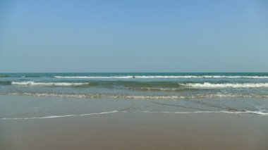 Deniz dalgaları, kumlu sahil ve mavi gökyüzü olan pitoresk bir marina.