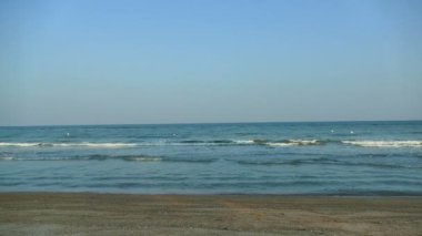 Deniz dalgaları, kumlu sahil ve mavi gökyüzü olan pitoresk bir marina.