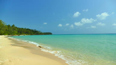 Deniz dalgaları, kumlu sahil ve mavi gökyüzü olan pitoresk bir marina.