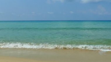 Deniz dalgaları, kumlu sahil ve mavi gökyüzü olan pitoresk bir marina.