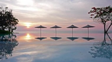Güneş şemsiyeleri ve deniz ve havuz üzerinde gün batımı manzarası