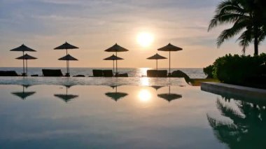 Güneş şemsiyeleri ve deniz ve havuz üzerinde gün batımı manzarası
