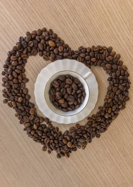 Taza de café y granos de café en una mesa de madera y forma de corazón hechos de granos de café —  Fotos de Stock