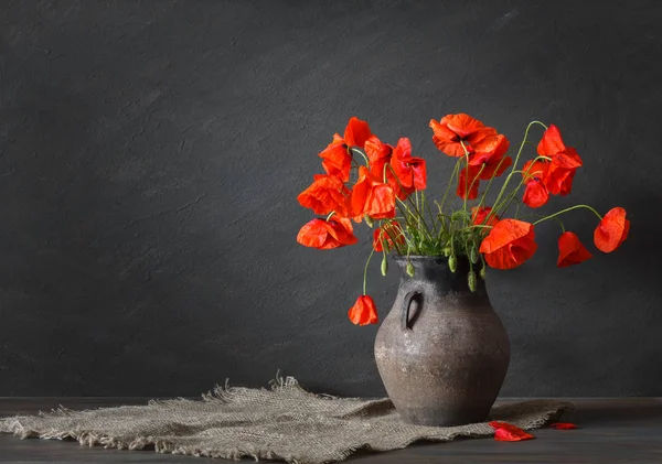 Naturaleza muerta en un estilo rústico: una vieja vasija y un ramo de amapolas sobre una mesa de madera — Foto de Stock