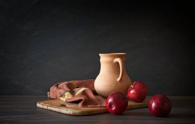 Rustik tarzı natürmort. Kırmızı elma ve kil sürahi ahşap bir masa üzerinde.