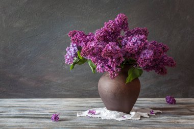 Durgun hayat. Ahşap bir masada kil bir sürahi içindeki leylak buketi. Kırsal biçim.