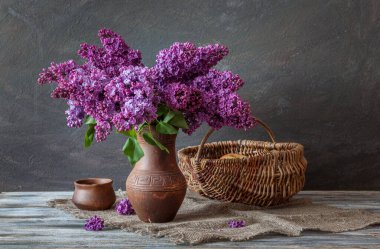 Sade bir yaşam tarzı. Ahşap bir masanın üzerinde bir demet leylak, hasır sepet ve çömlek..