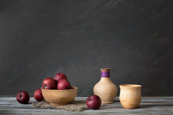 Still life in a rustic style. Set of ceramic dishes and red apples on a wooden table.