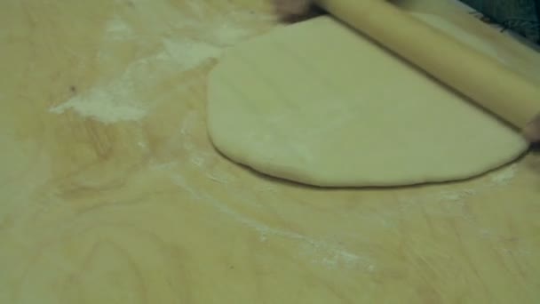 Una mujer está rodando la masa sobre una superficie de madera plana . — Vídeos de Stock