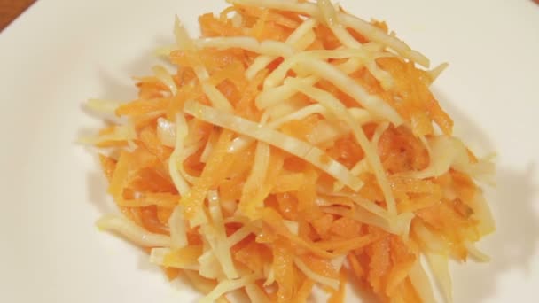 La ensalada vegetal de la zanahoria y la col en el plato blanco sobre el fondo de madera se acercan. Ensalada vegetariana saludable en aceite vegetal — Vídeos de Stock