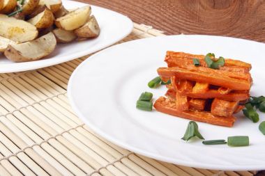 Havuç ve beyaz bir plaka üzerinde yeşil soğanlı patates pişmiş. Bambu hasır üzerinde organik sebzeli yemekler
