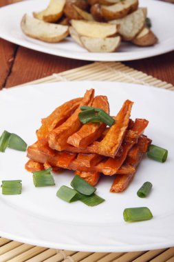 Pişmiş havuç ve patates ile beyaz bir plaka üzerinde yeşil soğan.