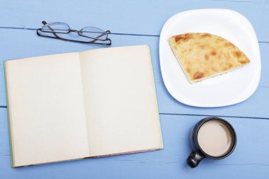 Beyaz sayfa, fincan kahve süt ve pasta ile ahşap masa üzerinde açık bir kitap. Kopya alanı veya tasarım eskiz. Kavram eğitim