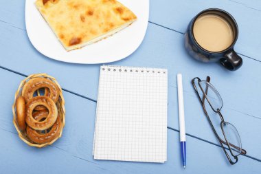 Not defteri yazma ve hafif kahvaltı için beyaz levha ile. Fincan sıcak çay veya kahve süt ve pasta. Mavi ahşap masa