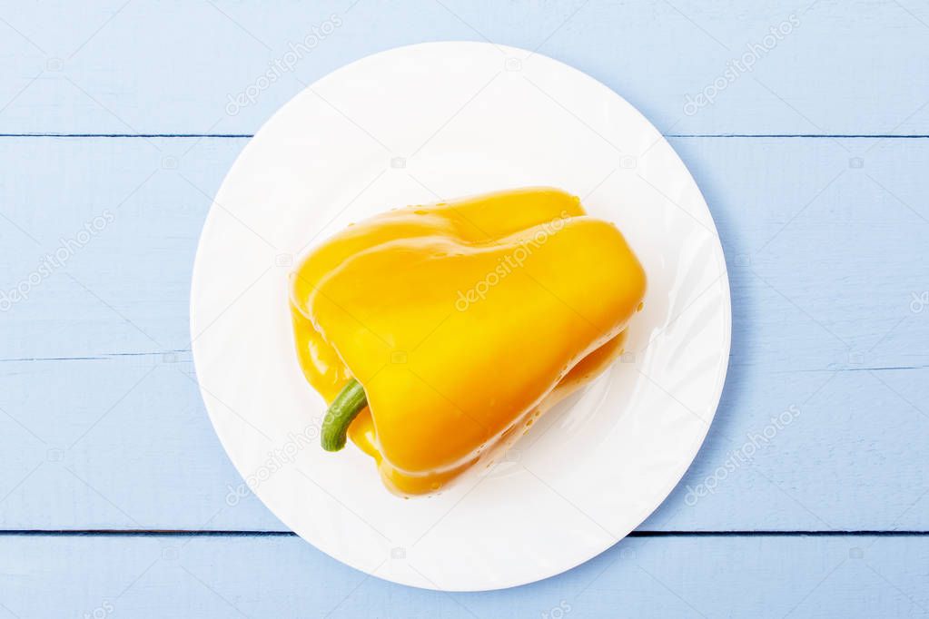 Ripe yellow whole bell pepper on white plate. Plate on wooden table. Organic vegetables for healthy food. Top view