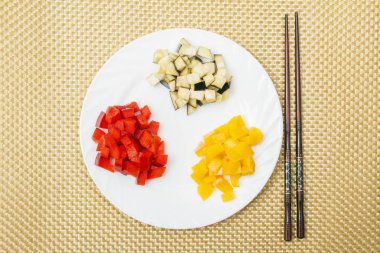 Taze kırmızı ve sarı tatlı biber ve patlıcan beyaz tabağa dilimlenmiş. Çin ve Japon yaşam tarzı. Sağlıklı gıda kavramı. Üstten Görünüm