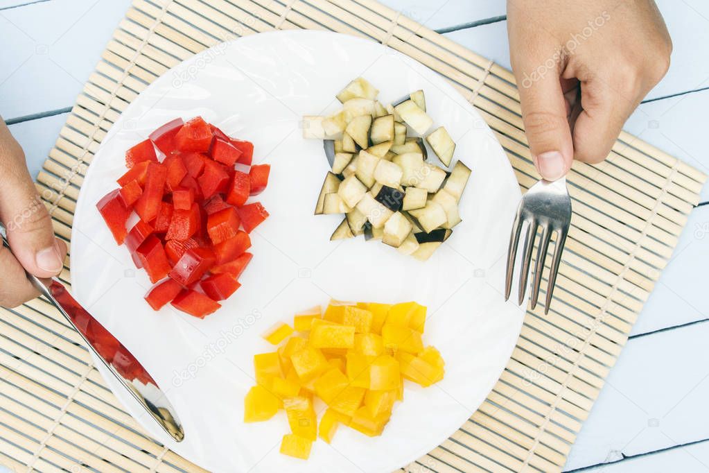 Vegetarian salad from organic vegetables on white plate. Chopped bell peppers and eggplant. Woman hands hold knife and fork. Chinese and japanese food concept