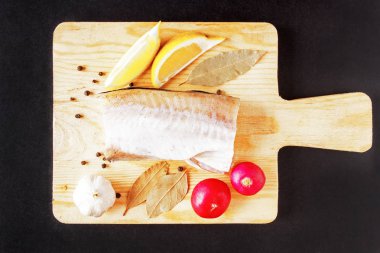 Pişmemiş Okyanus balık ve rustik ahşap kesme tahtası üzerinde siyah zemin üzerinde taze sebze. Üstten Görünüm