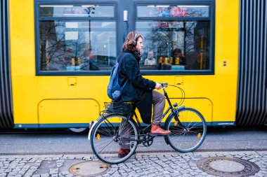 Berlin, Almanya - Aralık 2019: Berlin 'de sokak hayatı. Şık giyimli bir adam tramvayın yanında bisiklet sürüyor..