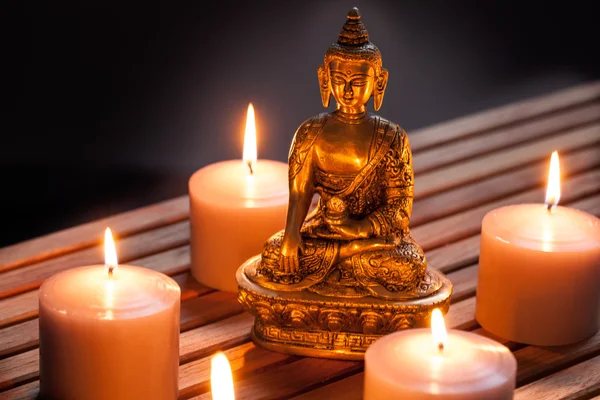 Bronze Buddha with warm lighted candles over wooden background — Stock Photo, Image