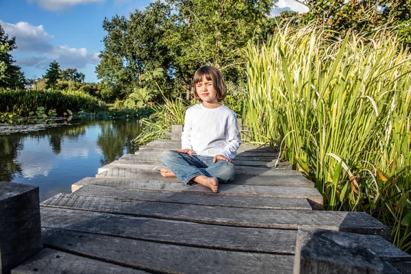 Relaxed child for yoga and meditation near water and trees — Stock Photo, Image