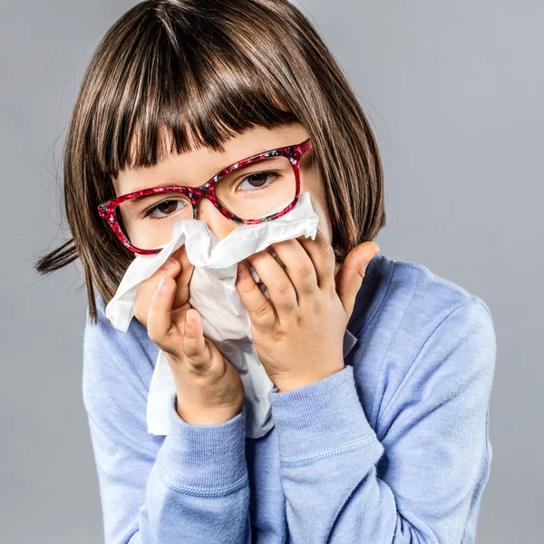 Sick young girl with eyeglasses blowing nose against cold — Stock Photo, Image